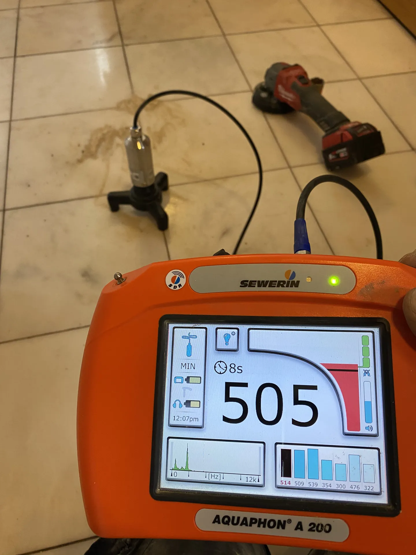 Acoustic leak detector with ground microphone on a tiled floor reading 505