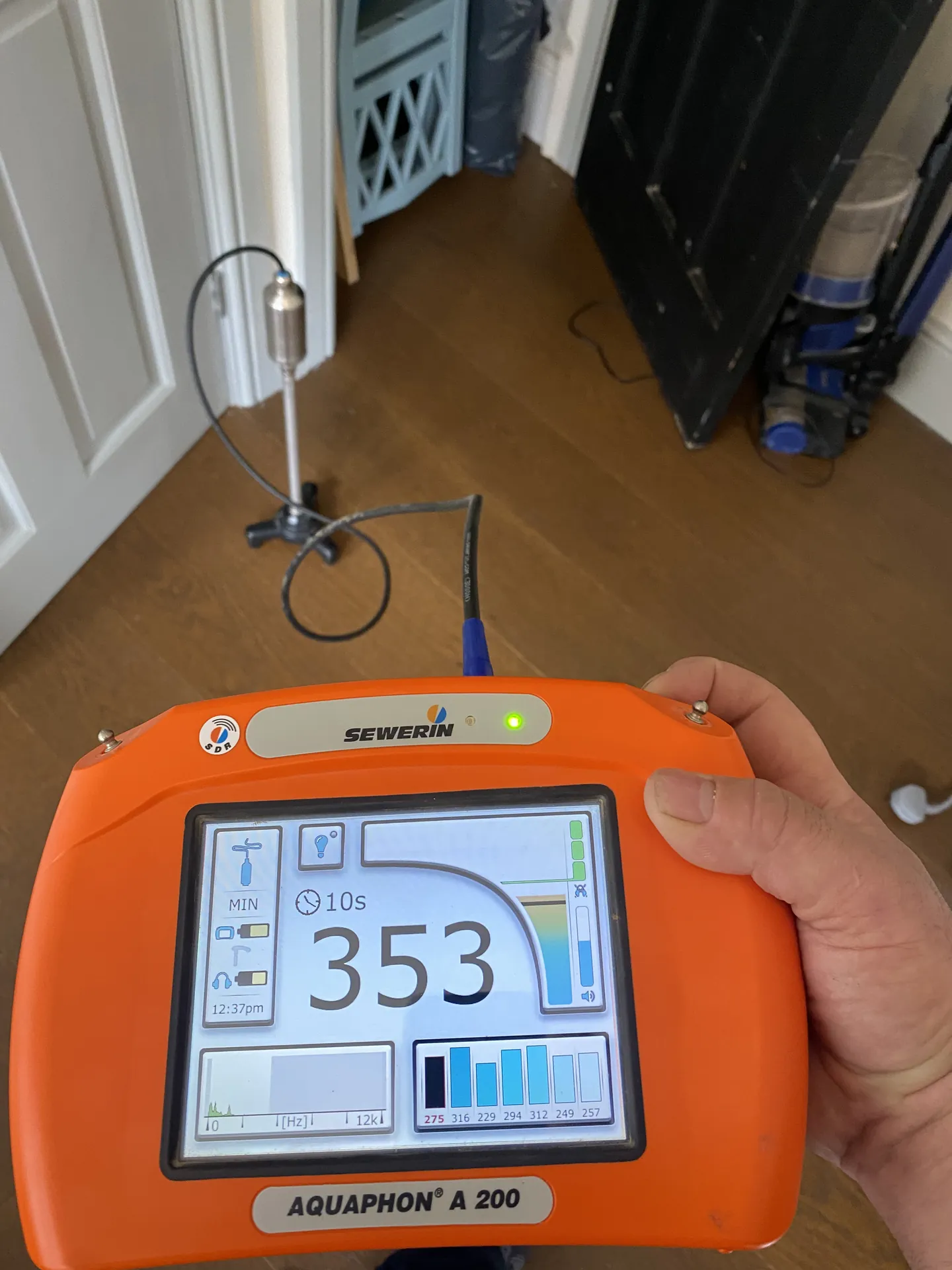 Acoustic leak detector held in the hand showing a reading of 353 in a hallway
