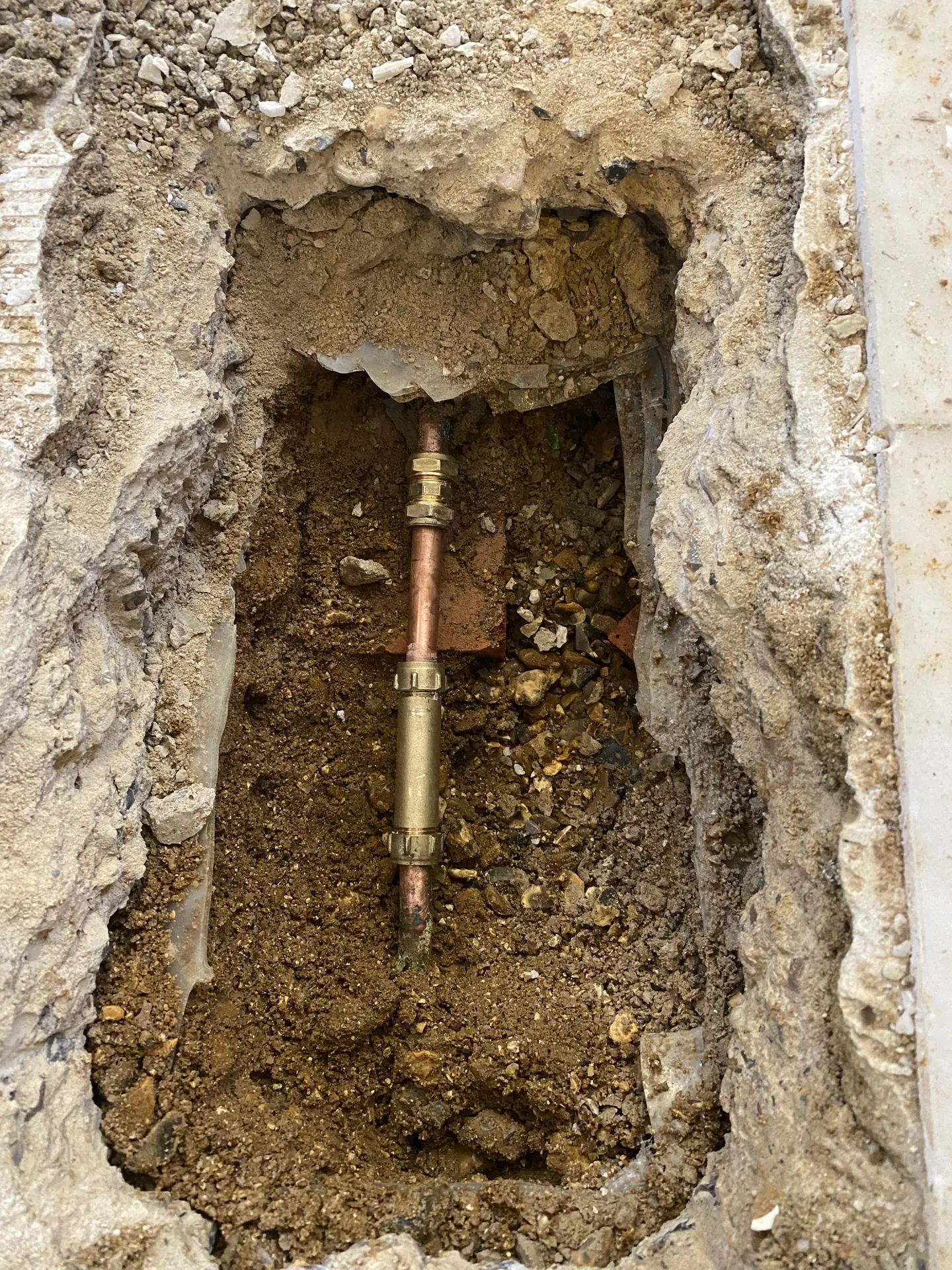 Copper supply pipe and stopcock exposed in a neat excavation through a concrete floor