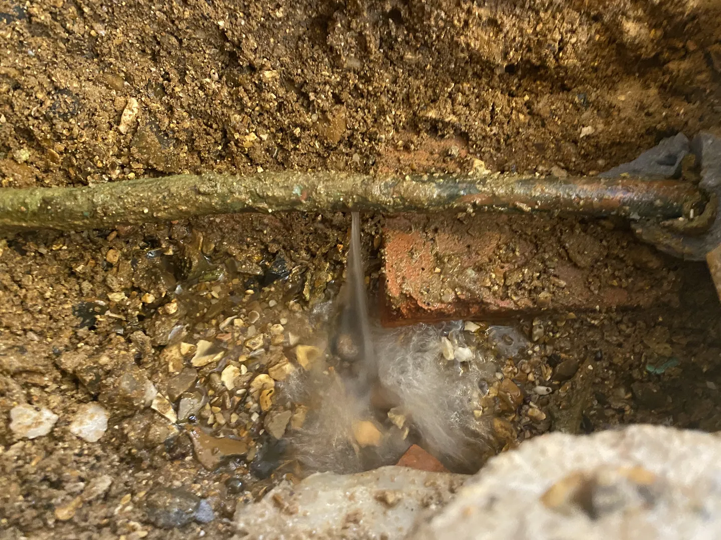 Corroded water pipe leaking in a small excavated trench