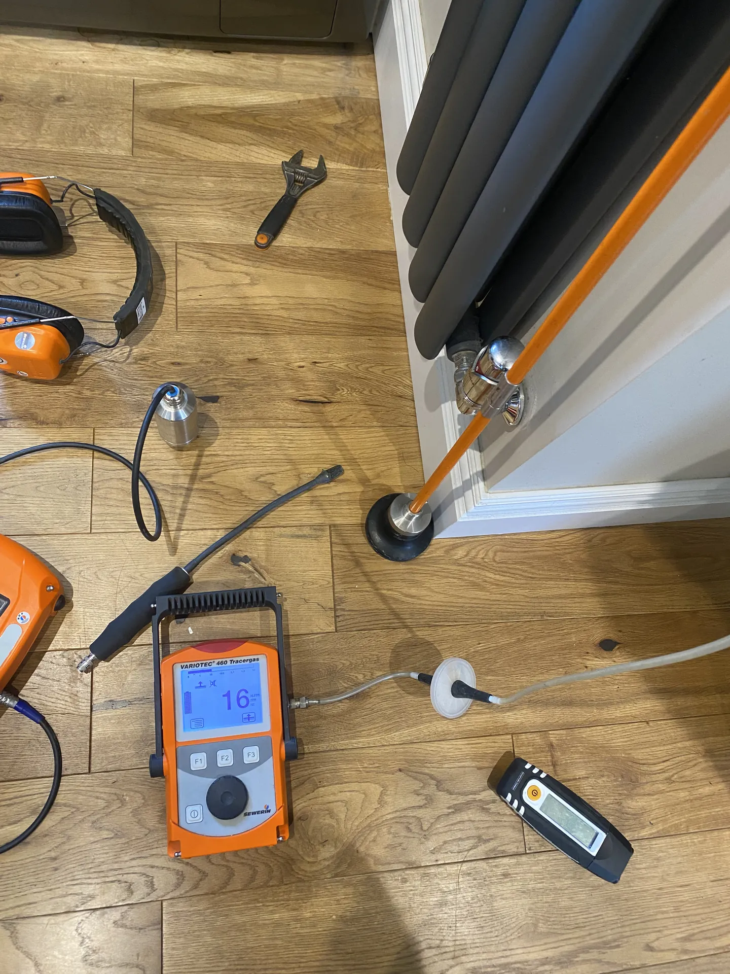 Tracer gas detector and tools on the floor beside a radiator during a heating leak survey