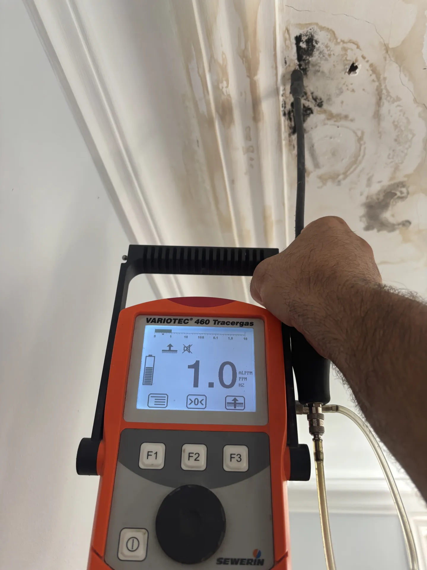 Tracer gas detector held against a damp patch on a painted wall