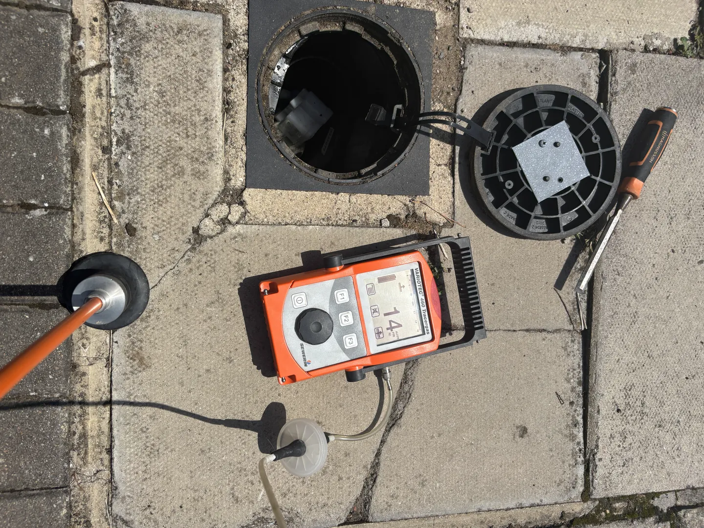 Tracer gas detector beside an open inspection chamber on a driveway