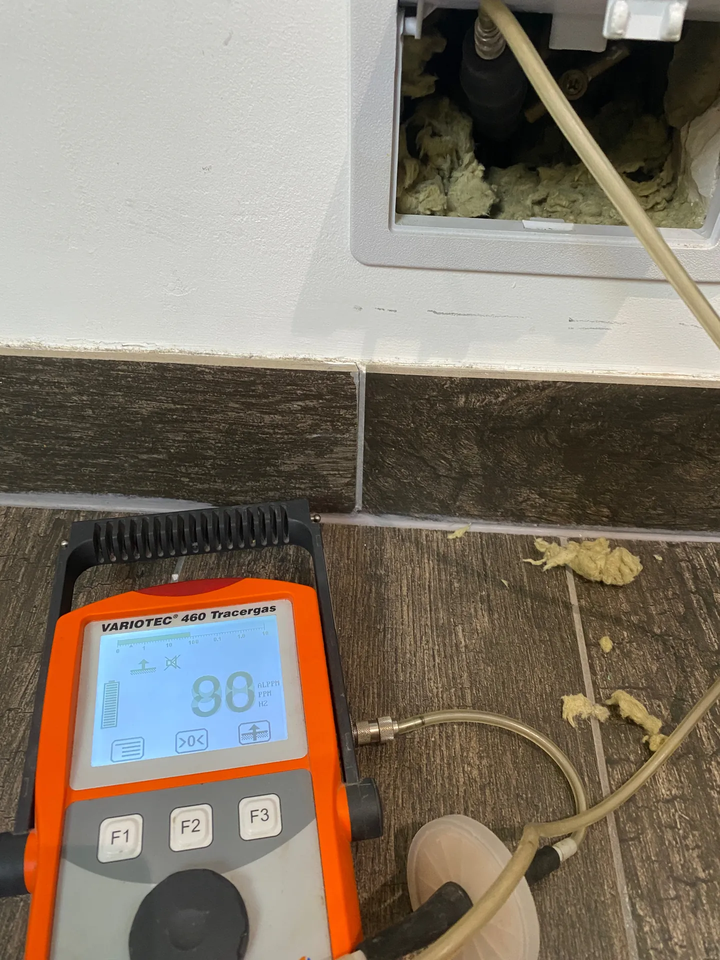 Tracer gas detector reading 96 at a pipe chase in a wall