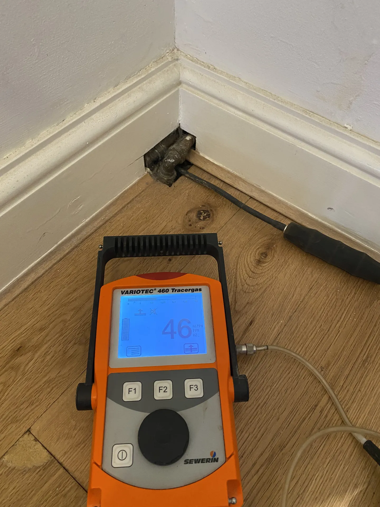 Tracer gas detector with its probe at a skirting board on a wooden floor