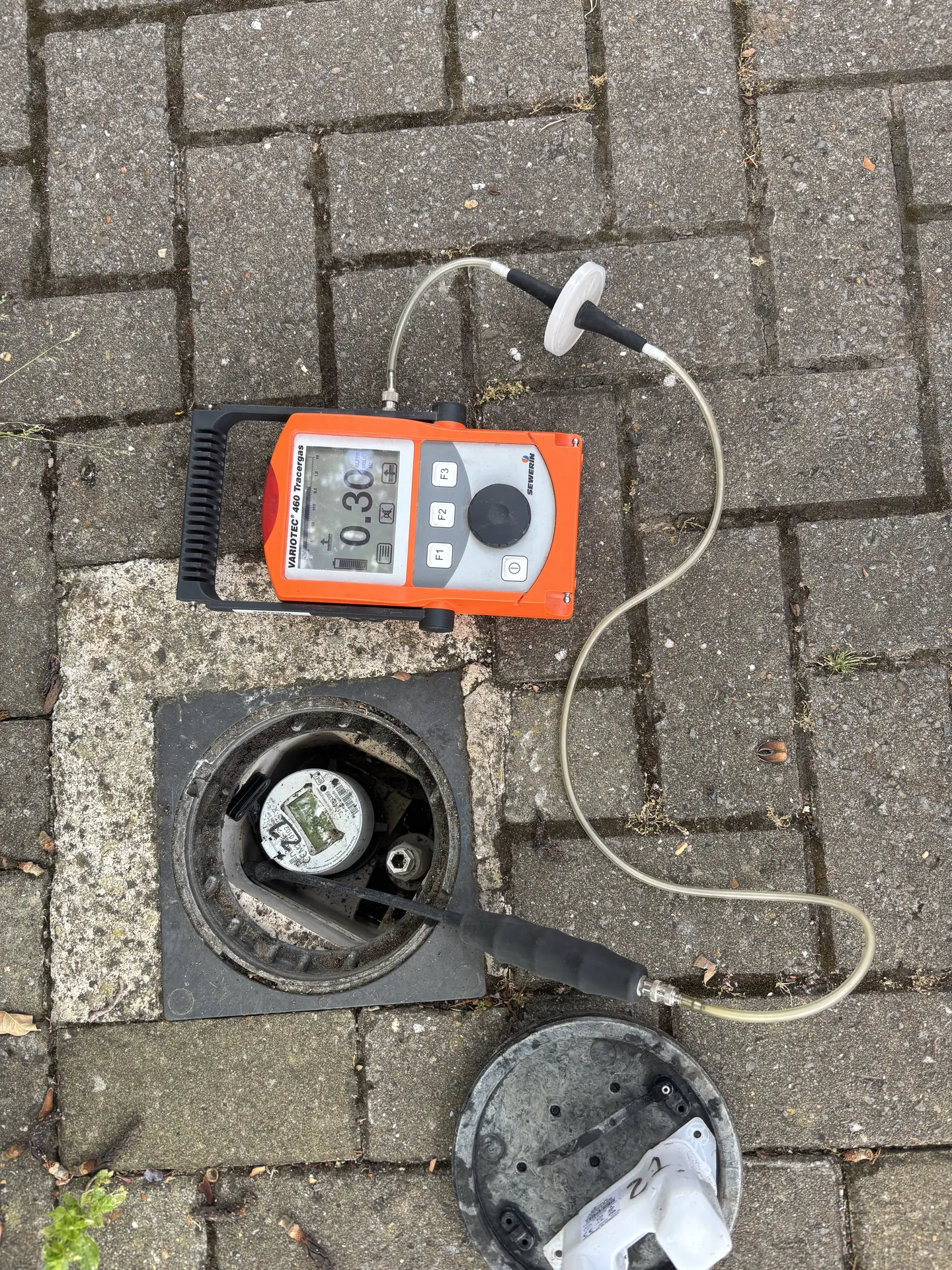 Tracer gas detector at an inspection chamber with the lid off on a paved drive